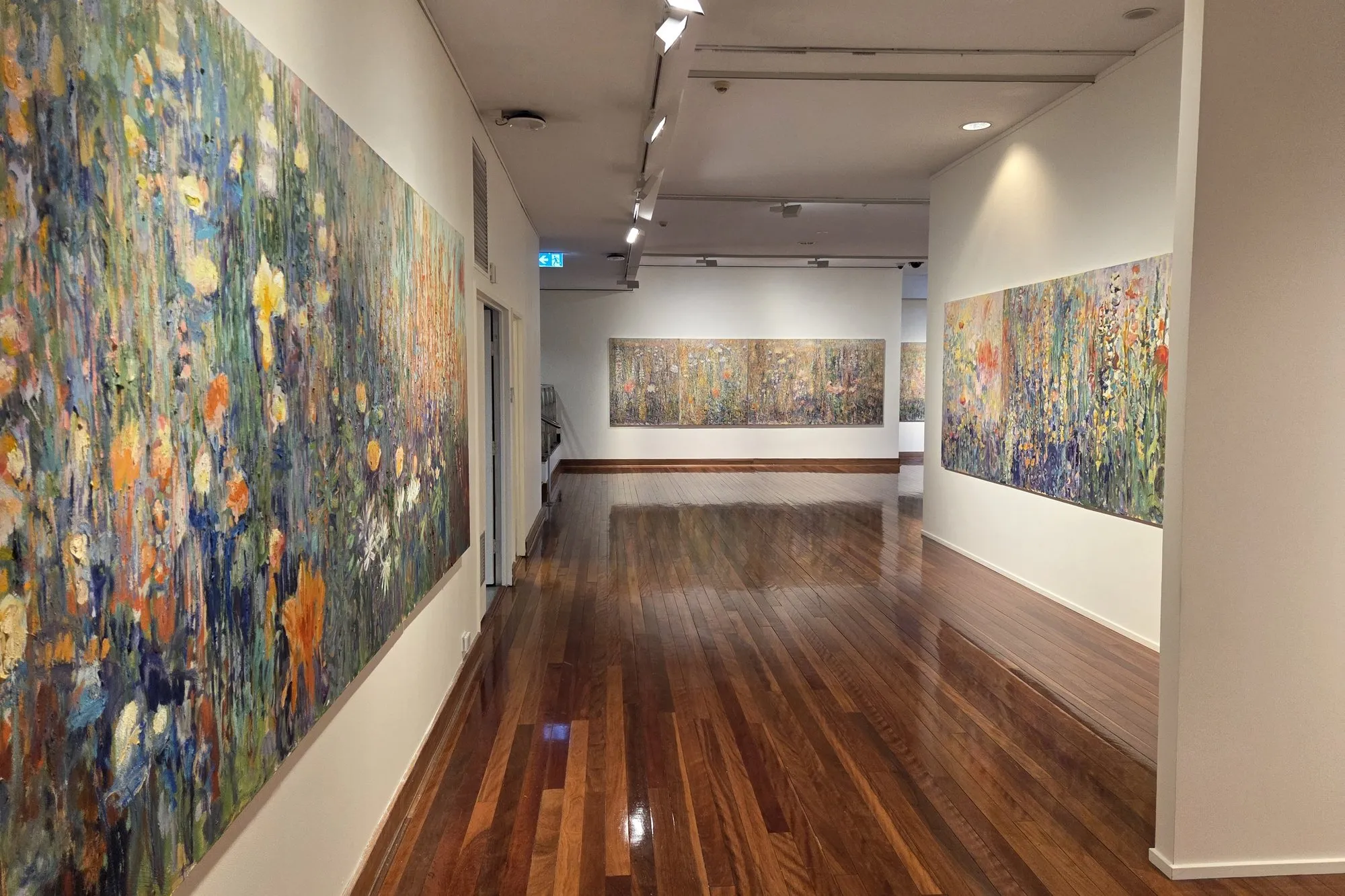 Large paintings installed along white gallery walls above a polished timber floor