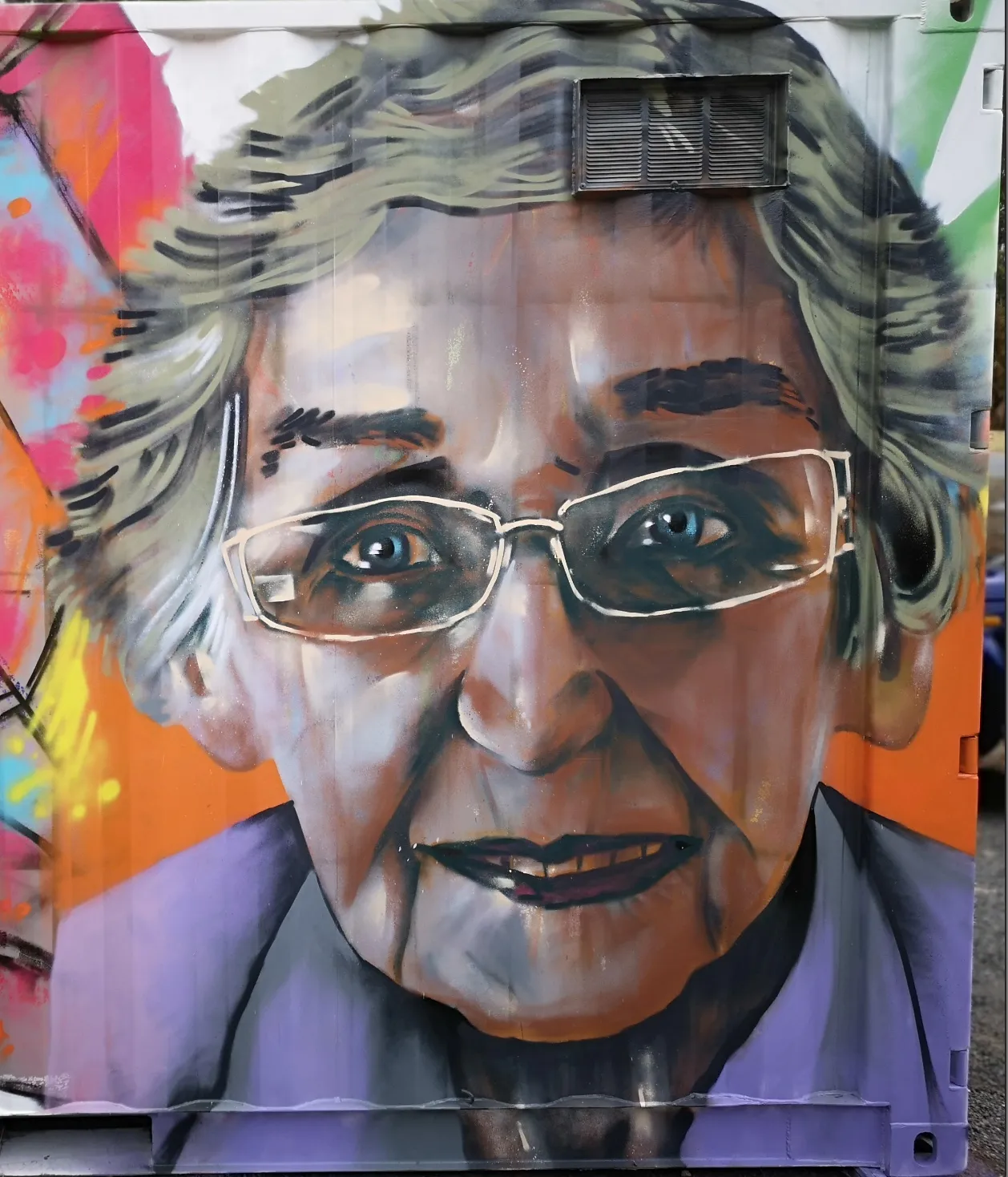 Portrait mural of an elderly woman wearing glasses, painted on the side of a shipping container