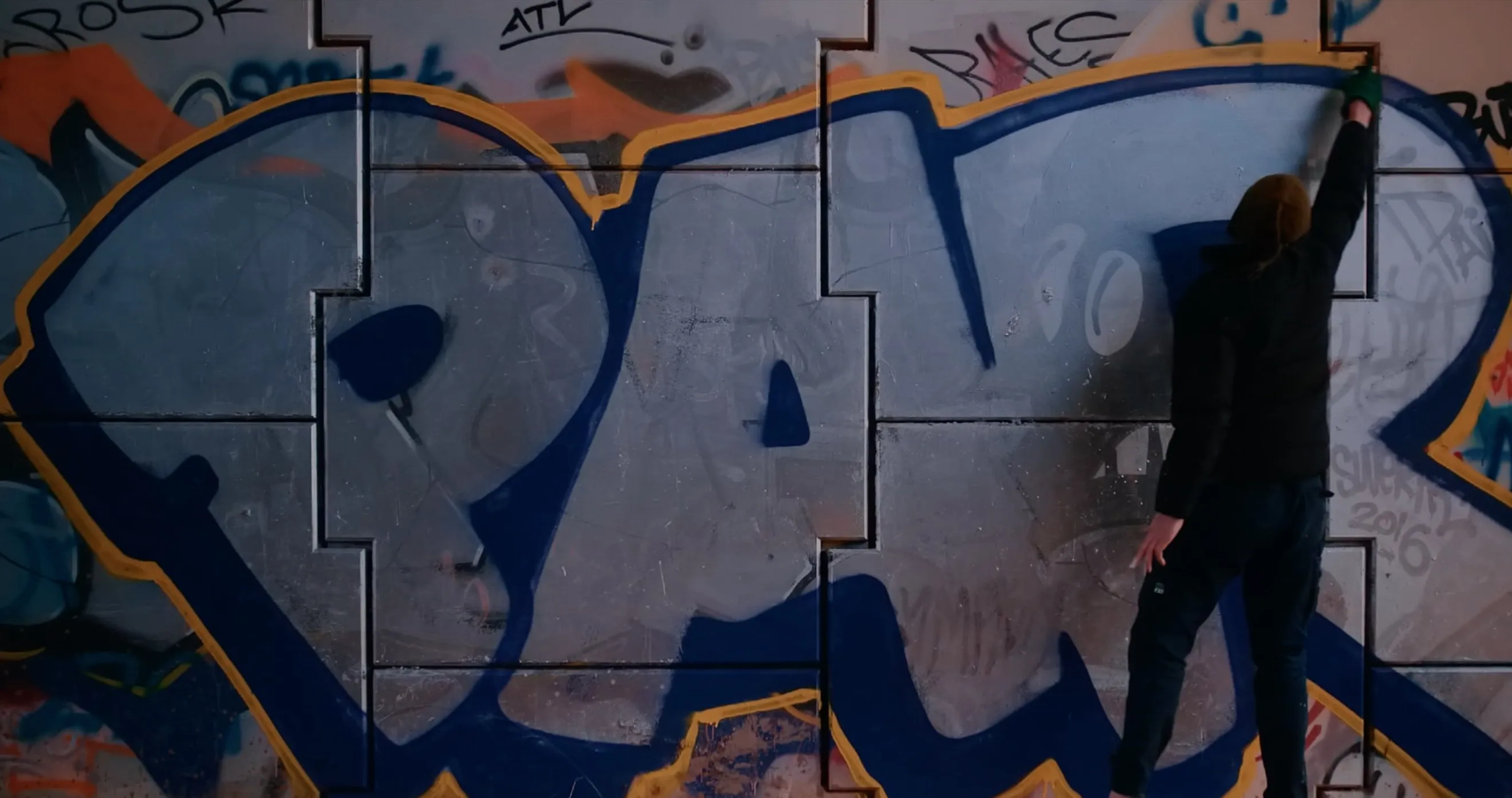 Artist painting a large blue and grey graffiti piece on a wall